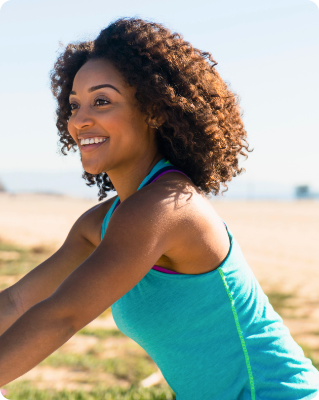 Smiling woman with curly hair in a turquoise vest top exercising outdoors in the sunshine