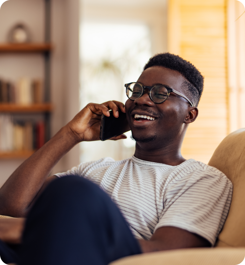 Smiling man wearing glasses relaxing on a sofa while talking on his mobile phone